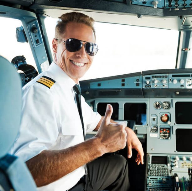 A man in a pilot's uniform and sunglasses smiles and gives a thumbs up.
